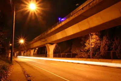 Elevated Skytrain guideway above a night road with street lamps and car light trails